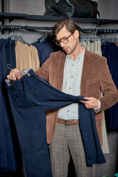 Homem bonito em óculos segurando cabide com calças elegantes na boutique — Fotografia de Stock