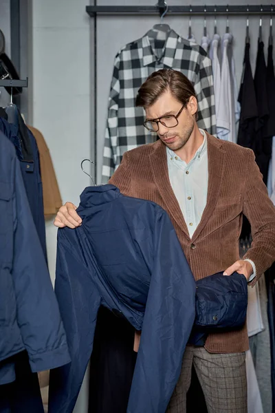 Handsome man in eyeglasses holding jacket while shopping in boutique — Stock Photo