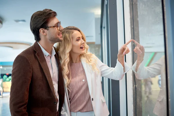 Sourire jeune couple regardant vitrine dans le centre commercial — Photo de stock