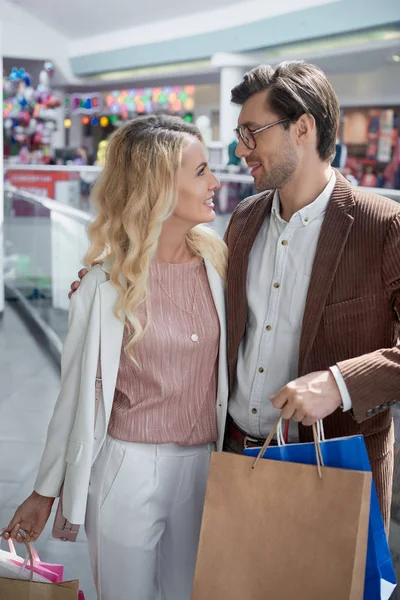Счастливая молодая пара с сумками, улыбающимися друг другу в торговом центре — стоковое фото