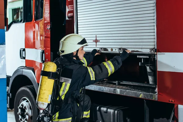 Feuerwehrfrau mit Feuerlöscher auf rückwärts schließendem Lastwagen am Feuerwehrhaus — Stockfoto