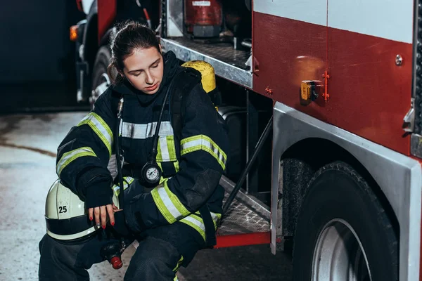 Tired female firefighter in uniform with helmet sitting on truck at fire station — Stock Photo
