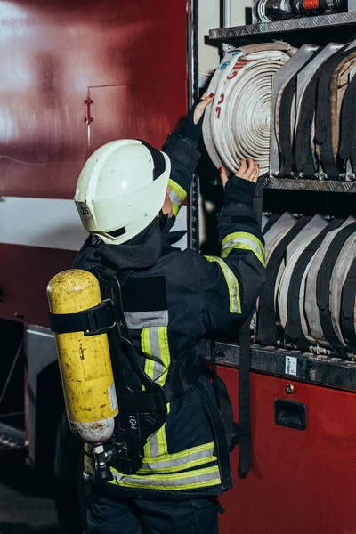 Vista parziale del vigile del fuoco femminile con estintore sul retro mettere tubo dell'acqua nel camion ai vigili del fuoco — Foto stock