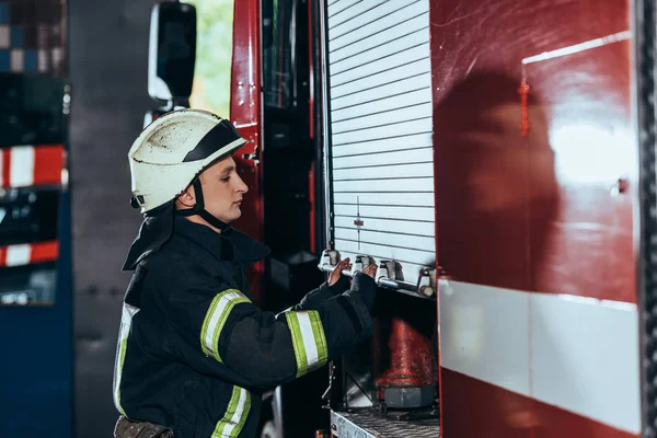 Вид збоку пожежника в уніформі закриваючої вантажівки в пожежному відділенні — стокове фото