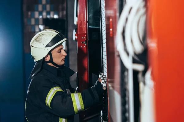 Vista lateral do bombeiro em caminhão de fechamento uniforme no corpo de bombeiros — Fotografia de Stock