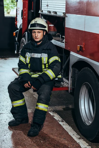 Male firefighter in uniform and helmet at fire truck at fire department — Stock Photo