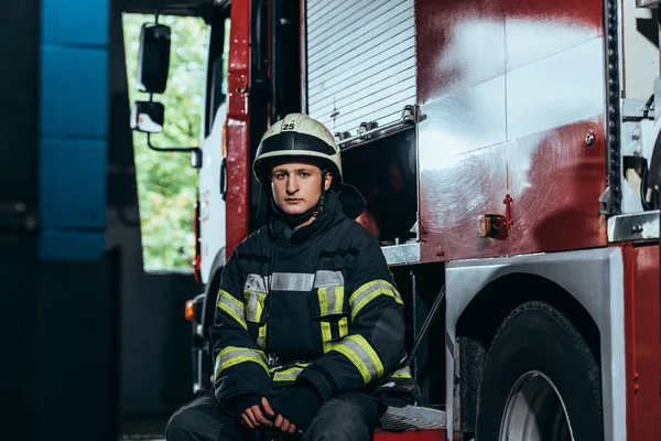 Retrato de bombero masculino en uniforme y casco en el departamento de bomberos de camiones de bomberos — Stock Photo