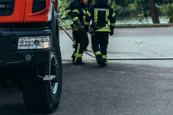 Partial view of brigade of firefighters and water hose on ground on street — Stock Photo