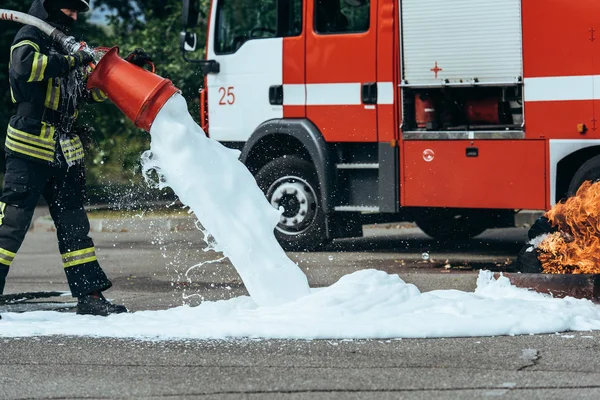 Partial view of firefighter extinguishing fire with foam on street — Stock Photo