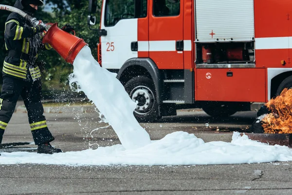 Visão parcial do bombeiro extinguindo fogo com espuma na rua — Fotografia de Stock