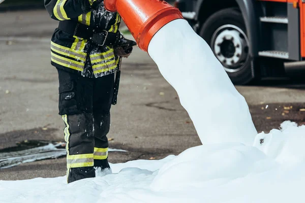 Cropped shot of firefighter extinguishing fire with foam on street — Stock Photo