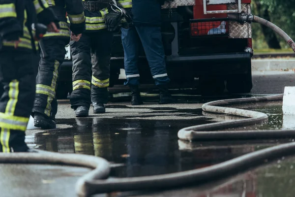 Vista parcial de la brigada de bomberos y manguera de agua en el suelo en la calle - foto de stock