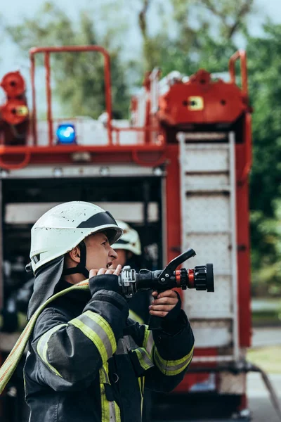 Selective focus of male firefighter in helmet with water hose on street — Stock Photo