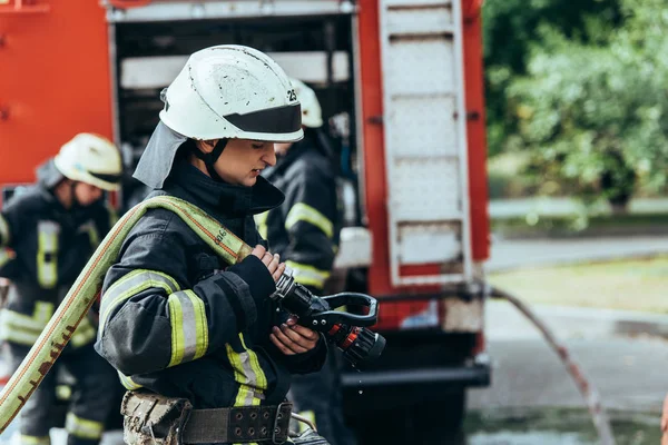 Foco seletivo de bombeiro masculino no capacete com mangueira de água na rua — Stock Photo