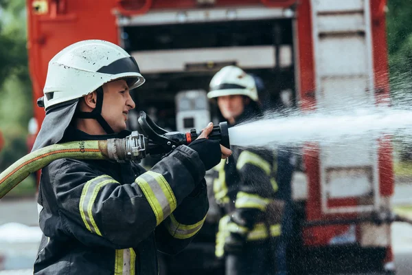 Foco seletivo do bombeiro com mangueira de água extinguindo incêndio na rua — Stock Photo