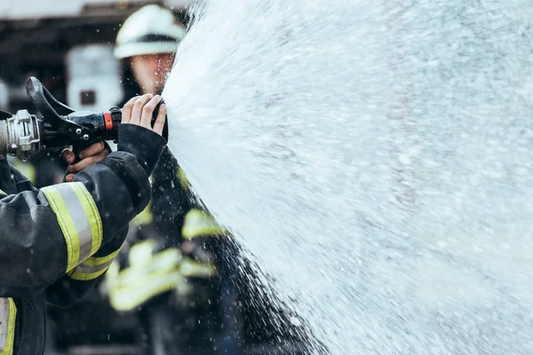Visão parcial do bombeiro com mangueira de água extinguindo incêndio na rua — Fotografia de Stock