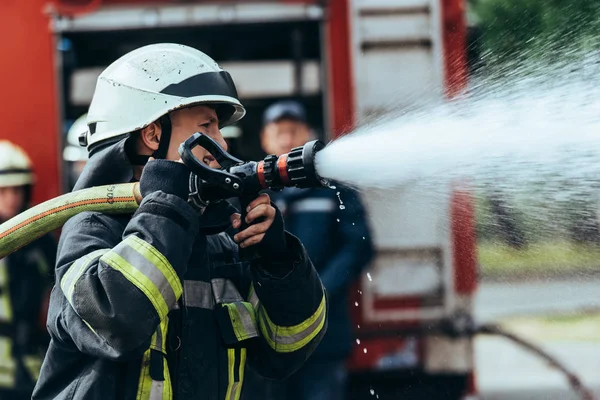 Foco seletivo do bombeiro com mangueira de água extinguindo incêndio na rua — Stock Photo