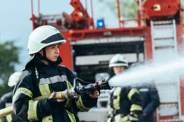 Bombero femenino con manguera de agua extinguiendo fuego en la calle - foto de stock