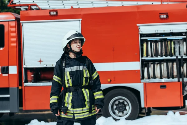 Bombeiro feminino em uniforme de proteção em pé na rua com caminhão de bombeiros vermelho atrás — Fotografia de Stock