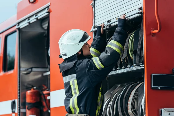 Side view of fire man closing truck with arranged water handes on street — стоковое фото