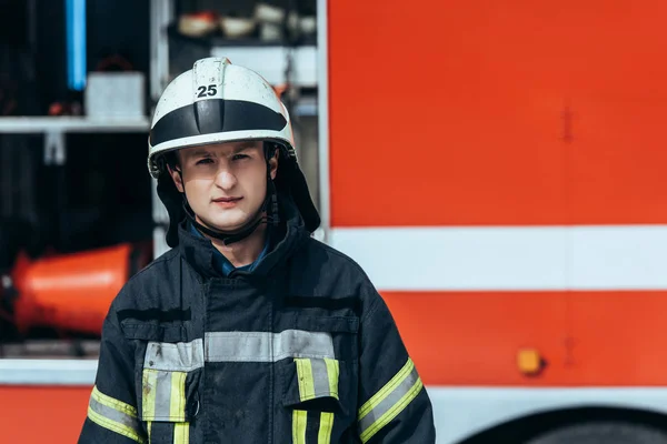 Retrato de bombero en uniforme de pie en la calle con camión de bomberos rojo detrás - foto de stock