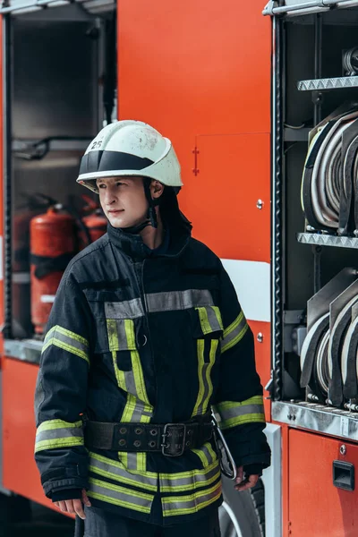 Feuerwehrmann mit Helm steht mit Wasserschläuchen an Lastwagen auf Straße — Stockfoto