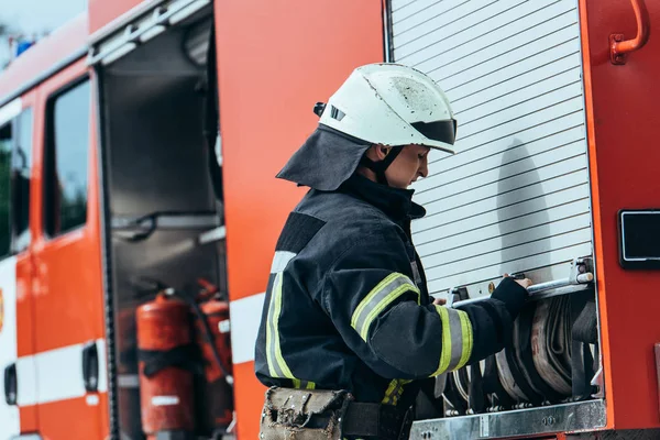 Side view of fireman closing truck with arranged water hoses on street — Stock Photo