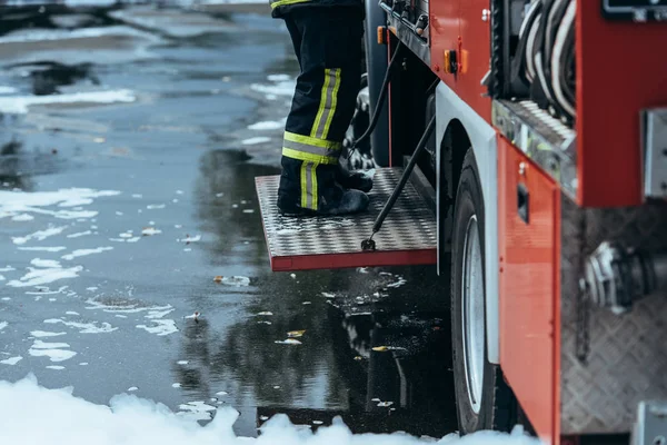 Tiro cortado de bombeiro em uniforme à prova de fogo em pé no caminhão de bombeiros na rua — Fotografia de Stock