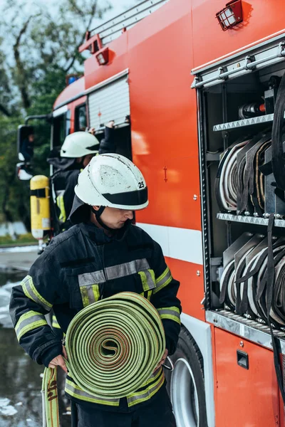 Bombero masculino poniendo manguera de agua en camión en la calle - foto de stock