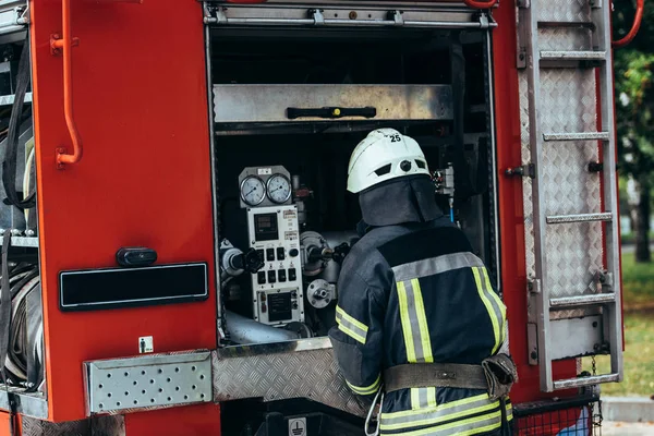 Вид ззаду пожежника в уніформі і шоломі, що стоїть на пожежній машині на вулиці — стокове фото