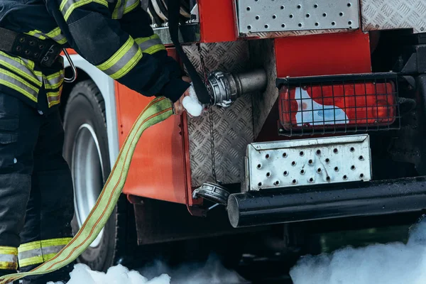 Vista parcial del bombero en la manguera de agua de control uniforme de protección - foto de stock