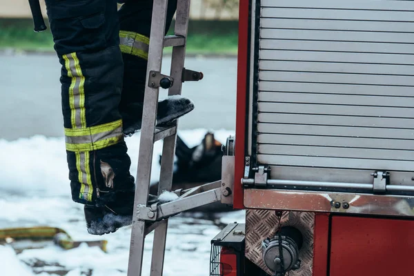 Disparo recortado de bombero en uniforme de protección de pie en la escalera de camiones en la calle - foto de stock