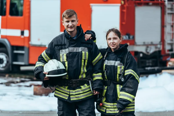 Portrait of firefighters in fireproof uniform standing on street with fire truck behind — Stock Photo