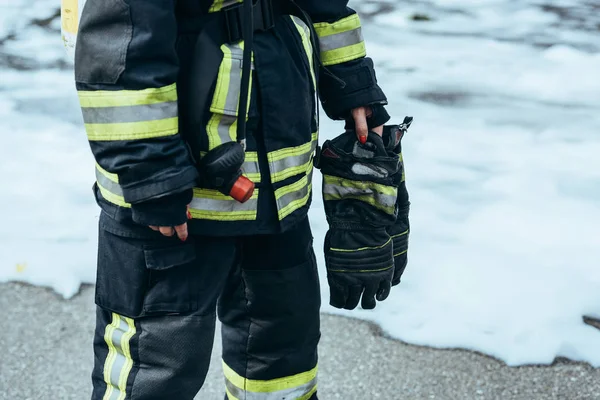 Teilaufnahme einer Feuerwehrfrau in feuerfester Uniform mit Handschuhen in der Hand, die auf einem Steg mit Schaumstoff steht — Stockfoto