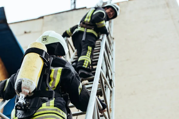 Foco seletivo de bombeiros em uniforme à prova de fogo em pé na escada — Fotografia de Stock