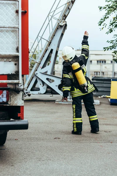 Вид ззаду пожежника в уніформі і шоломі з вогнегасником на задньому жесті на вулиці — стокове фото