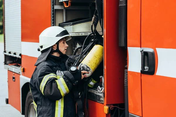 Feuerwehrfrau in Schutzuniform steckt Feuerlöscher in Lastwagen auf Straße — Stockfoto