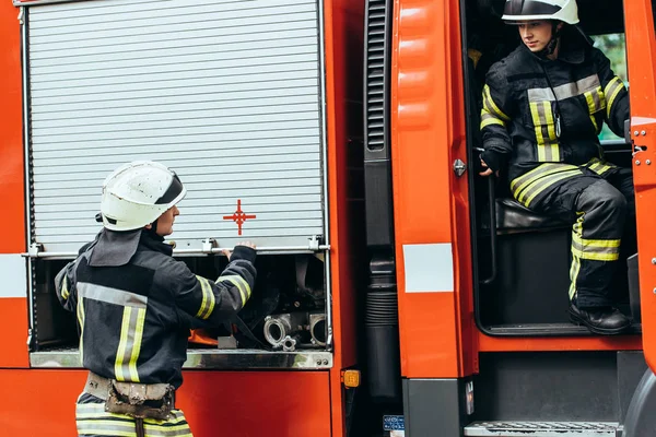 Firefighters in protective uniform and helmets at fire truck on street — Stock Photo