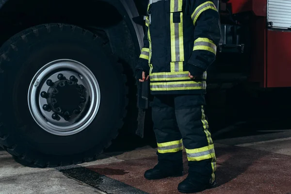 Частичный обзор пожарного в защитной огнеупорной форме, стоящего у пожарной станции — стоковое фото