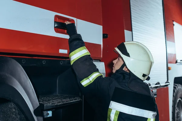 Вид збоку жіночого пожежника, який тримає ручку дверей вантажівки у пожежному відділенні — стокове фото