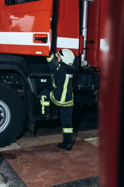 Female firefighter in protective uniform getting into truck at fire station — Stock Photo