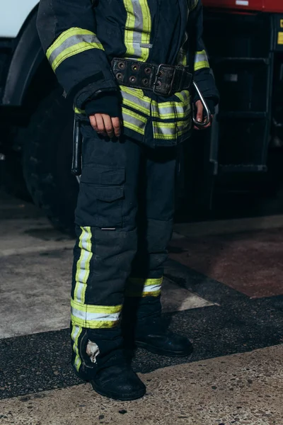 Частичное представление пожарного в защитной огнеупорной униформе, стоящей у пожарной части — стоковое фото