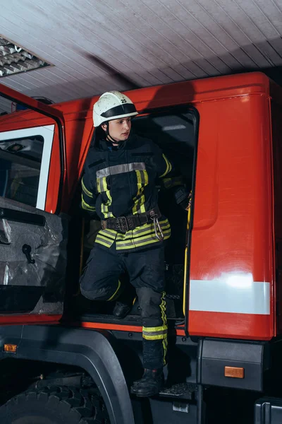 Пожежник в захисній формі і шолом вилітає з вантажівки на пожежній станції — стокове фото