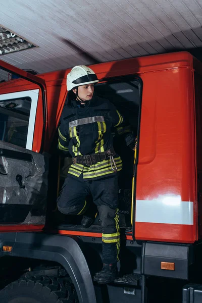 Fireman in protective uniform and helmet getting out of truck at fire station — Stock Photo