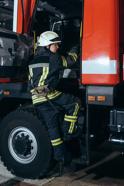 Bombeiro em uniforme de proteção e capacete entrar no caminhão no quartel de bombeiros — Fotografia de Stock
