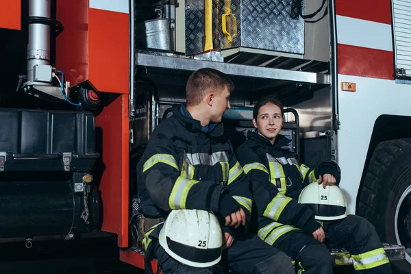 Pompiers en uniforme de protection ayant une conversation près du camion à la caserne de pompiers — Photo de stock