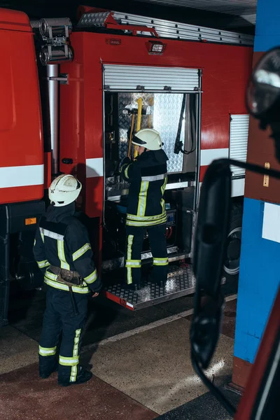 Partial view of firefighters in fireproof uniform and helmets at fire station — Stock Photo