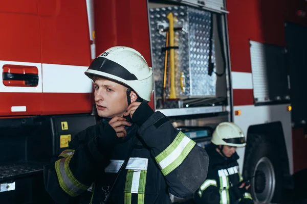 Firefighter checking helmet with colleague behind at fire department — Stock Photo