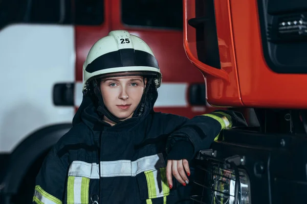 Porträt einer Feuerwehrfrau mit Helm, die sich am Feuerwehrhaus auf einen Lastwagen stützt — Stockfoto