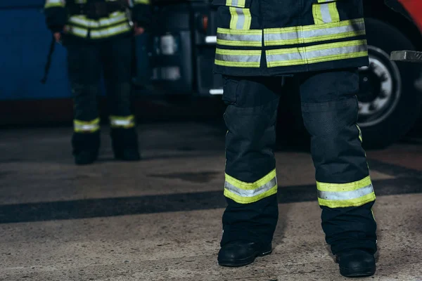 Visão parcial de bombeiros em uniforme à prova de fogo de proteção em pé no quartel de bombeiros — Fotografia de Stock